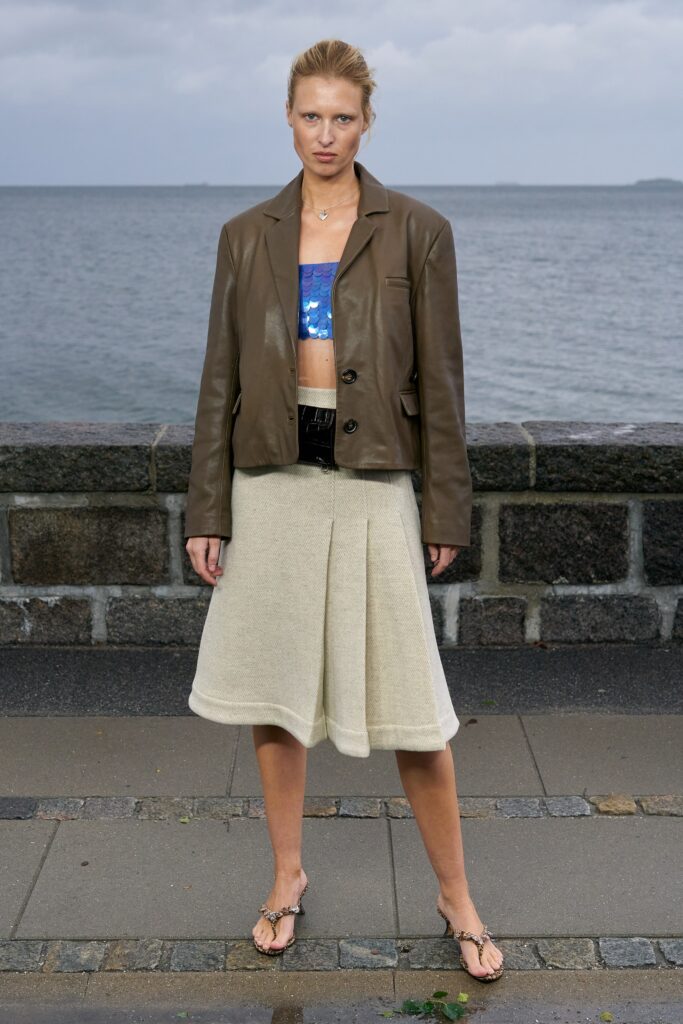 A fitted brown leather jacket paired with a pleated beige skirt, creating a stylish ensemble.