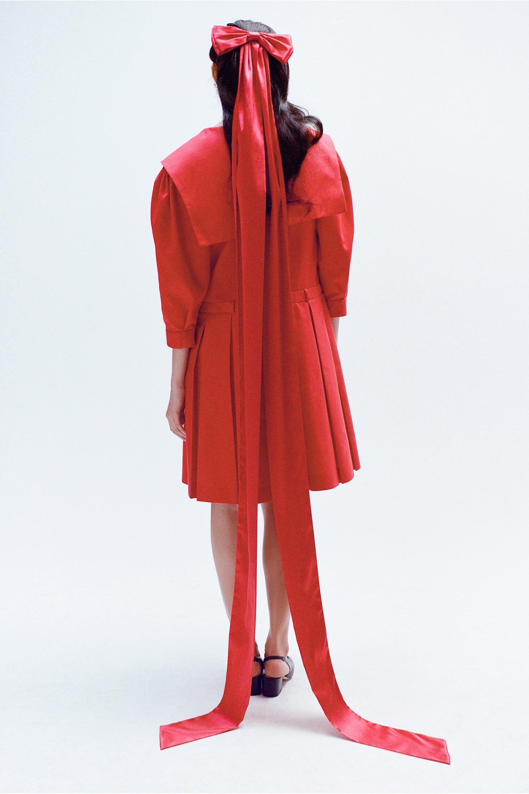 A relaxed red cotton dress with short sleeves, a collared neckline, and pleated details.