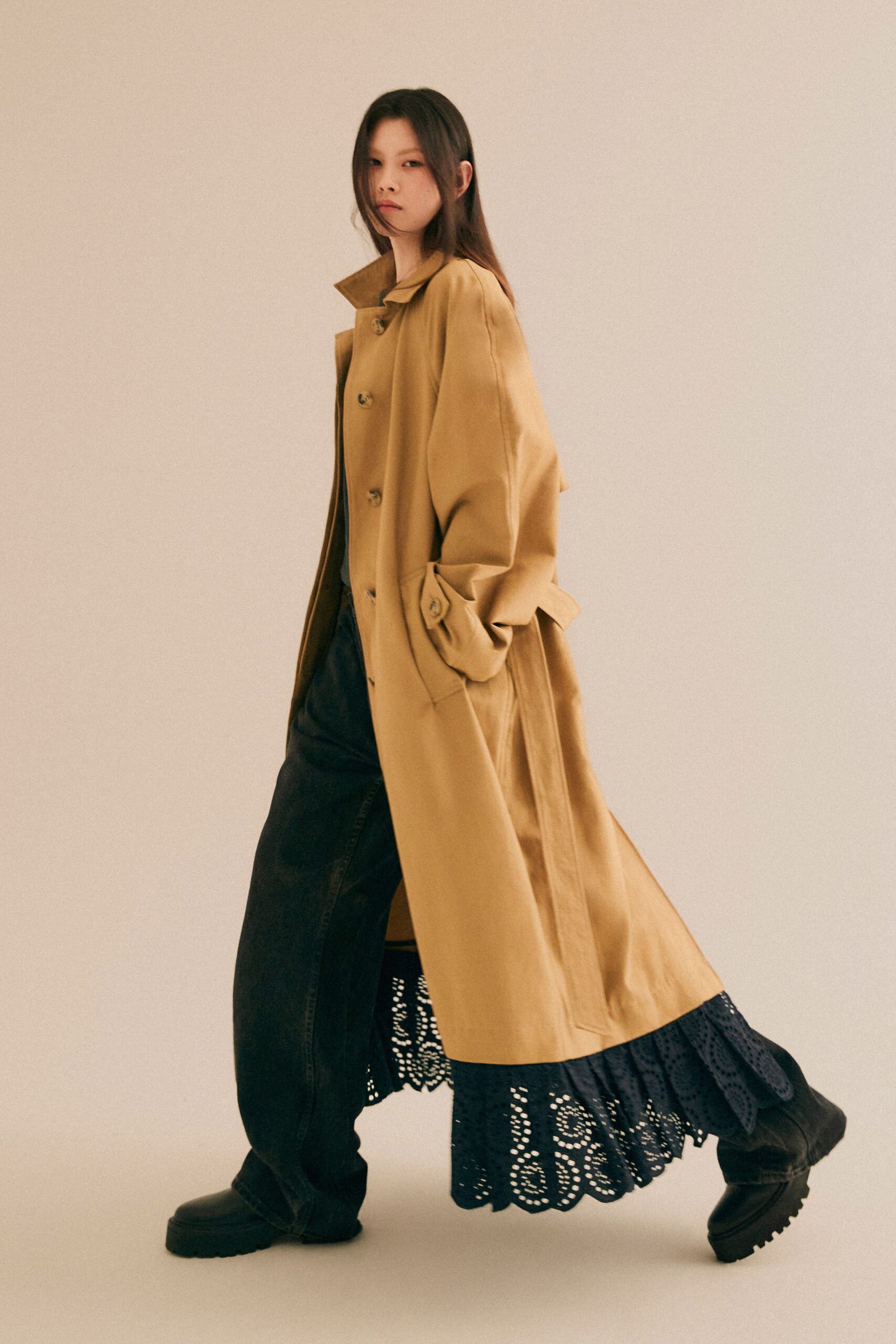 A relaxed beige coat paired with black lace layered pants for a stylish look.