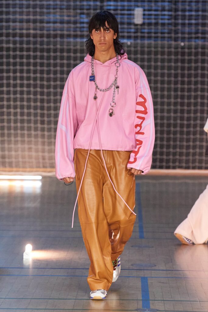 A relaxed pink hoodie with a hood and printed details paired with brown leather pants.
