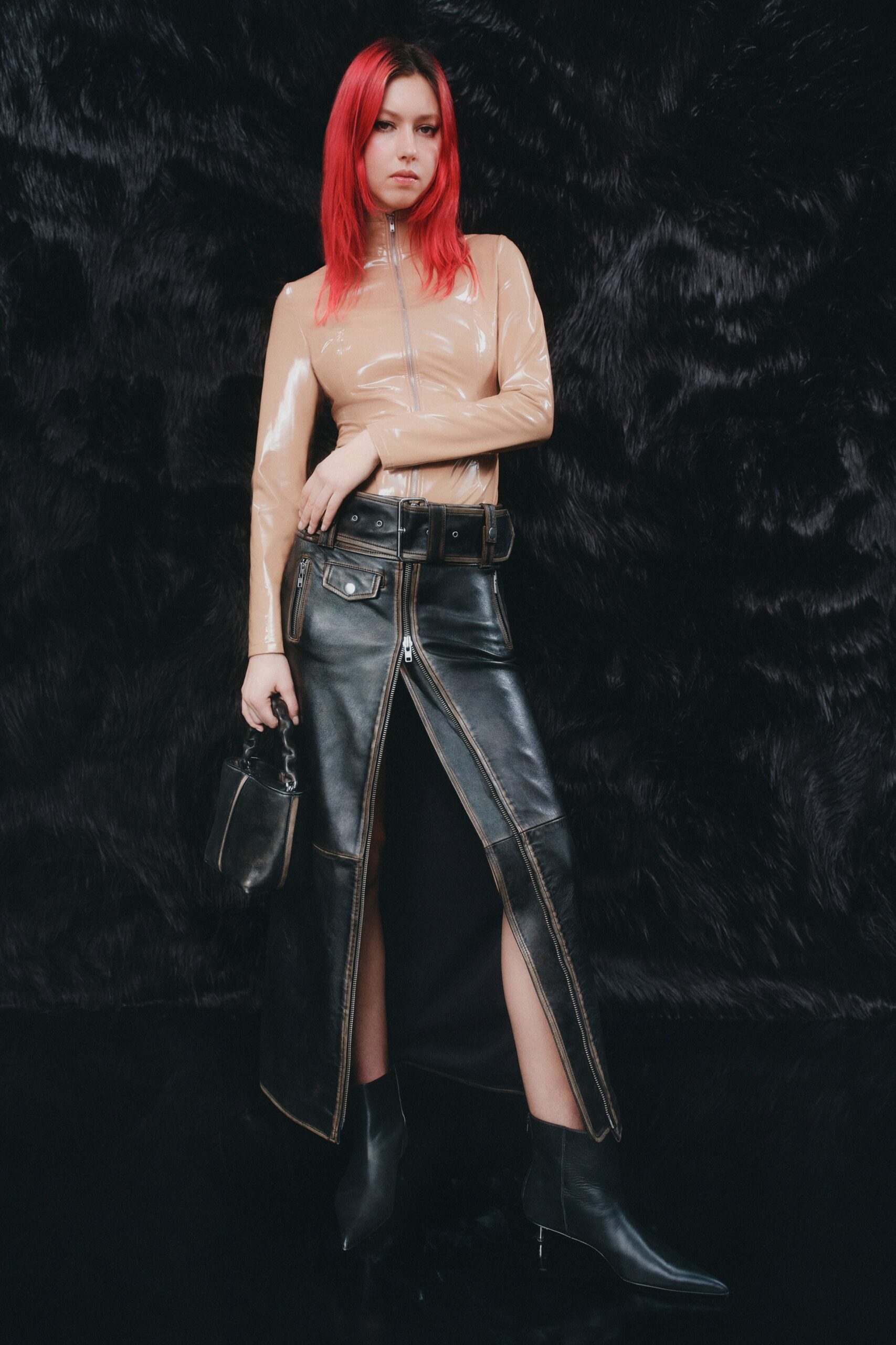A fitted black leather skirt with a slit paired with a beige long-sleeve top featuring a high neckline.