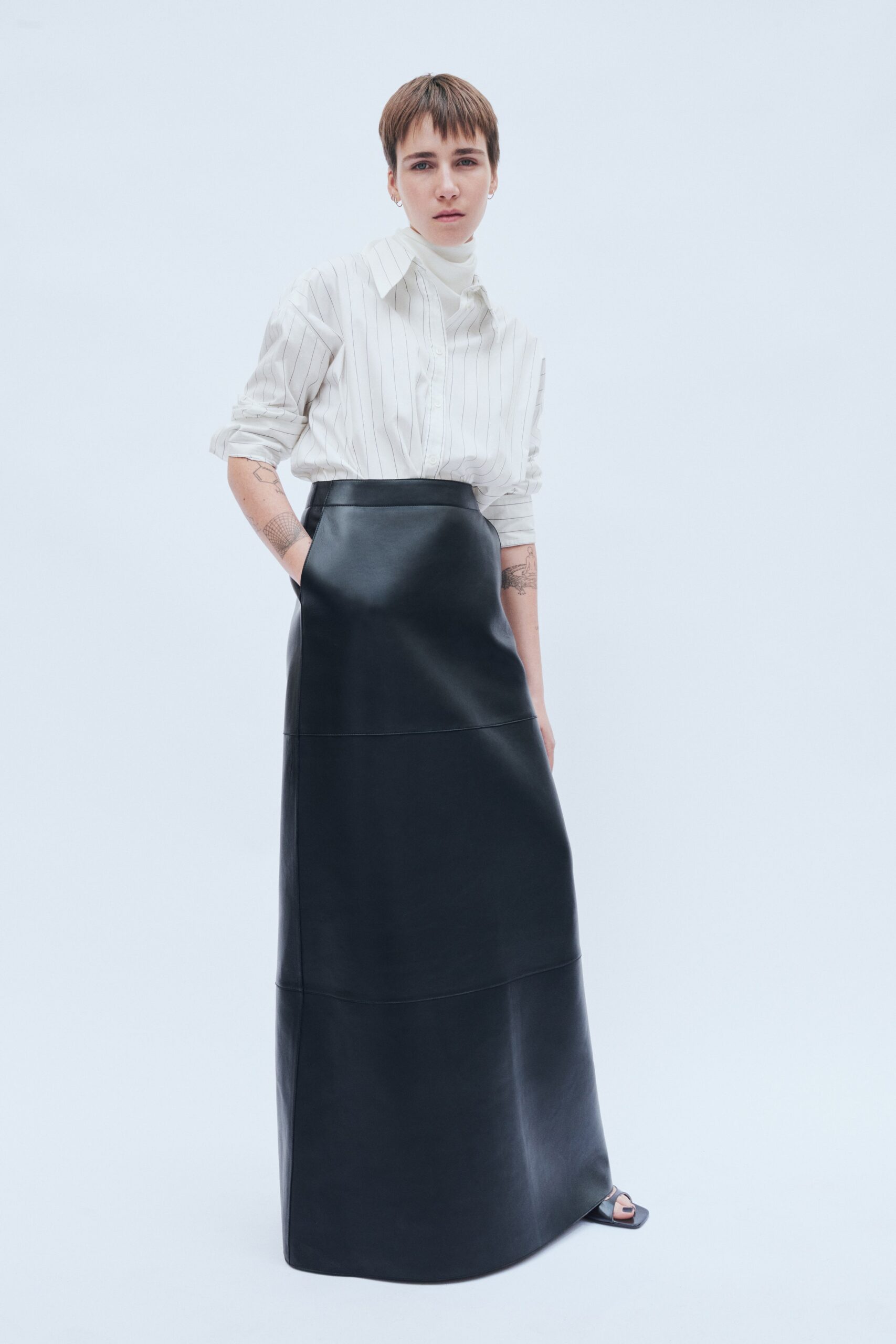 A fitted black leather skirt paired with a long-sleeve collared striped shirt.