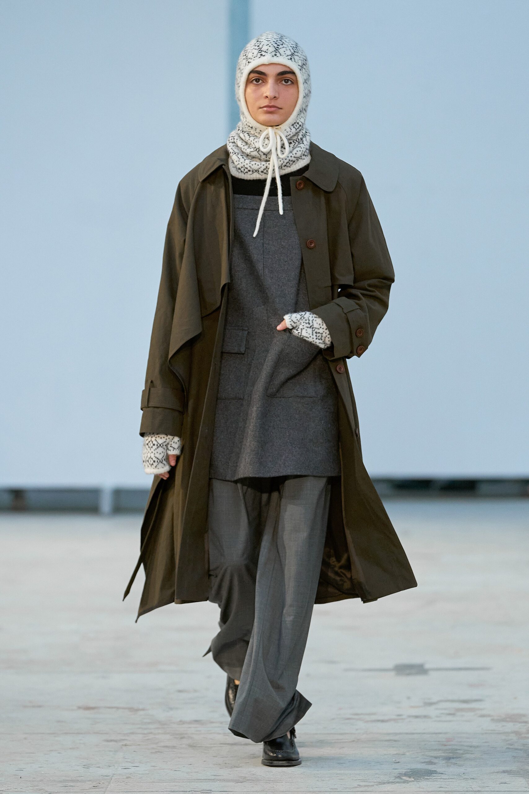 A relaxed olive coat paired with gray pants, featuring a long-sleeve and collared design.