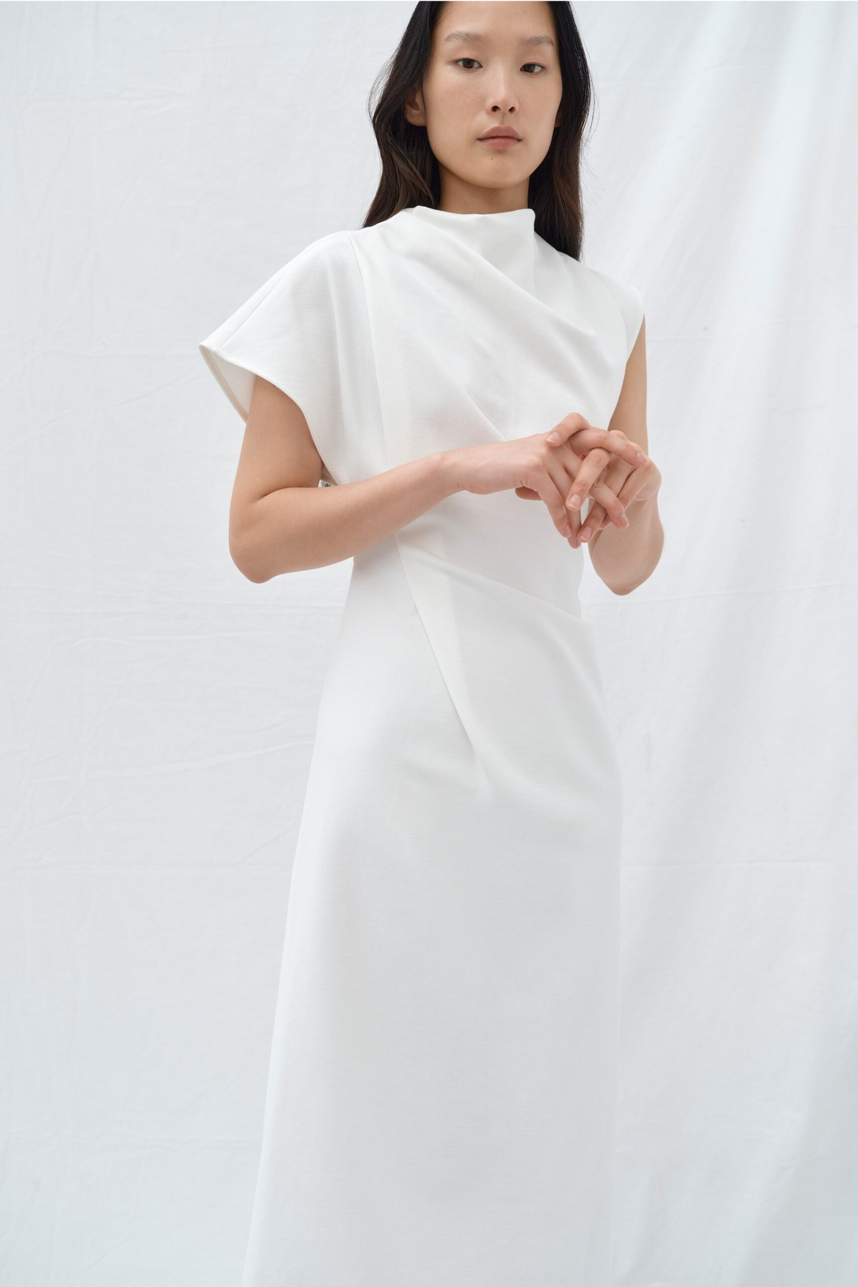 A fitted white dress with an asymmetric design and high-neck construction.