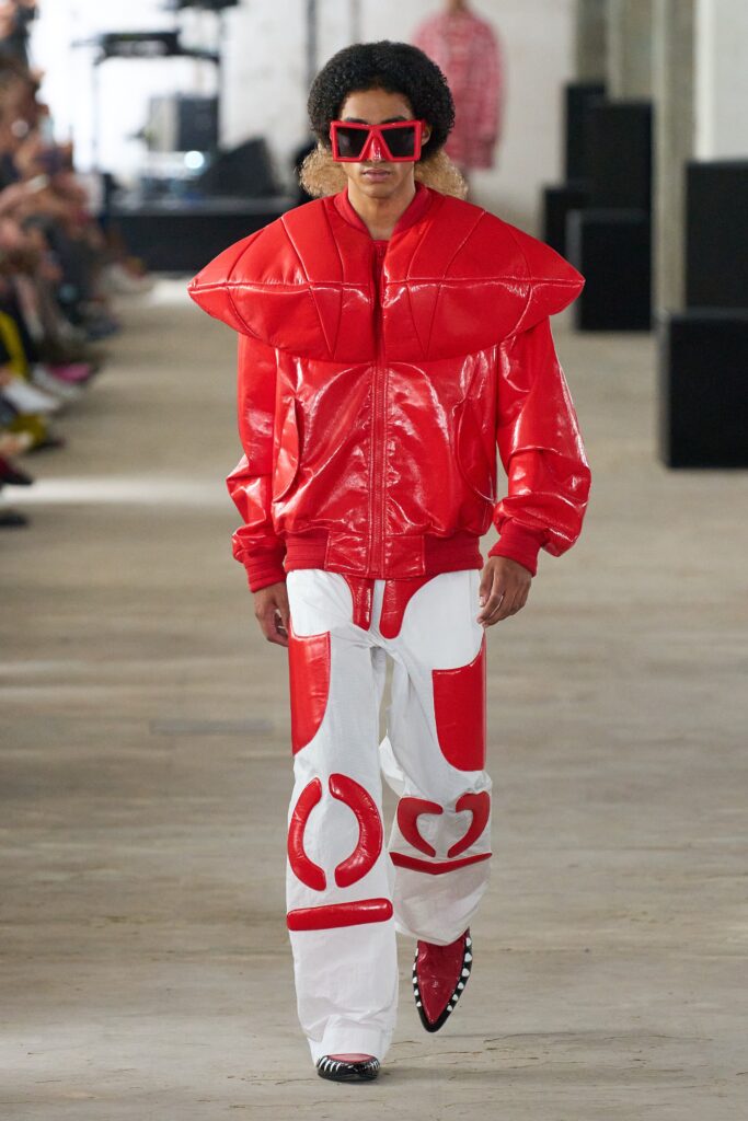 A fitted red leather jacket with an asymmetric design paired with white leather pants.