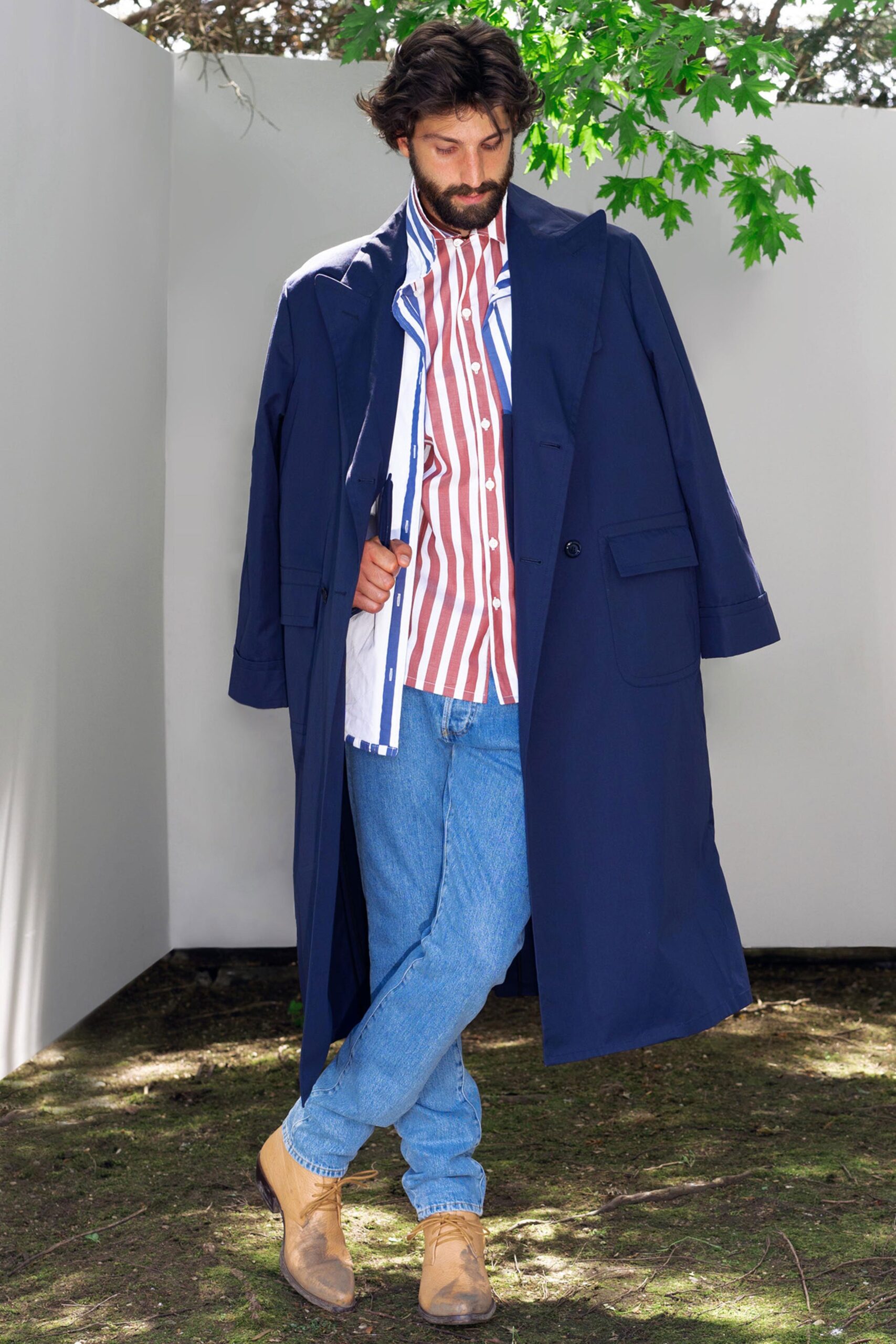 A relaxed blue coat layered over a collared long-sleeve striped shirt.