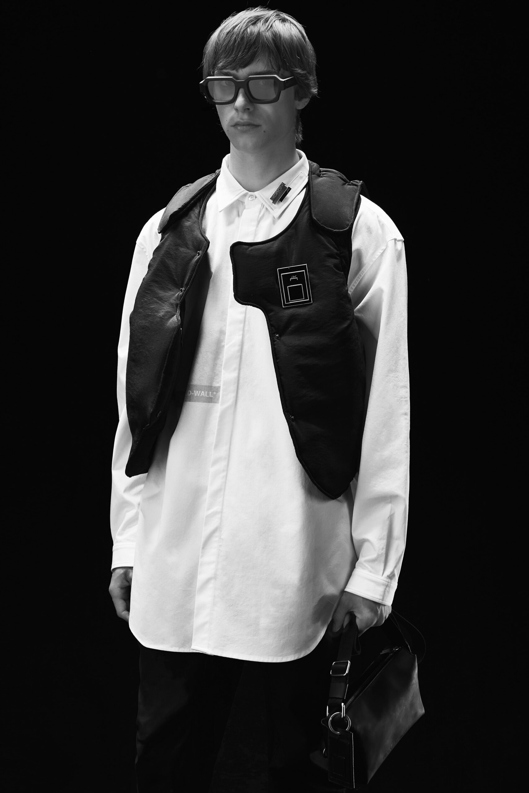 This ensemble features a relaxed white shirt layered beneath a striking black leather vest. The combination of textures creates a compelling visual contrast, while the long sleeves and collar of the shirt add a classic touch to the contemporary layering.