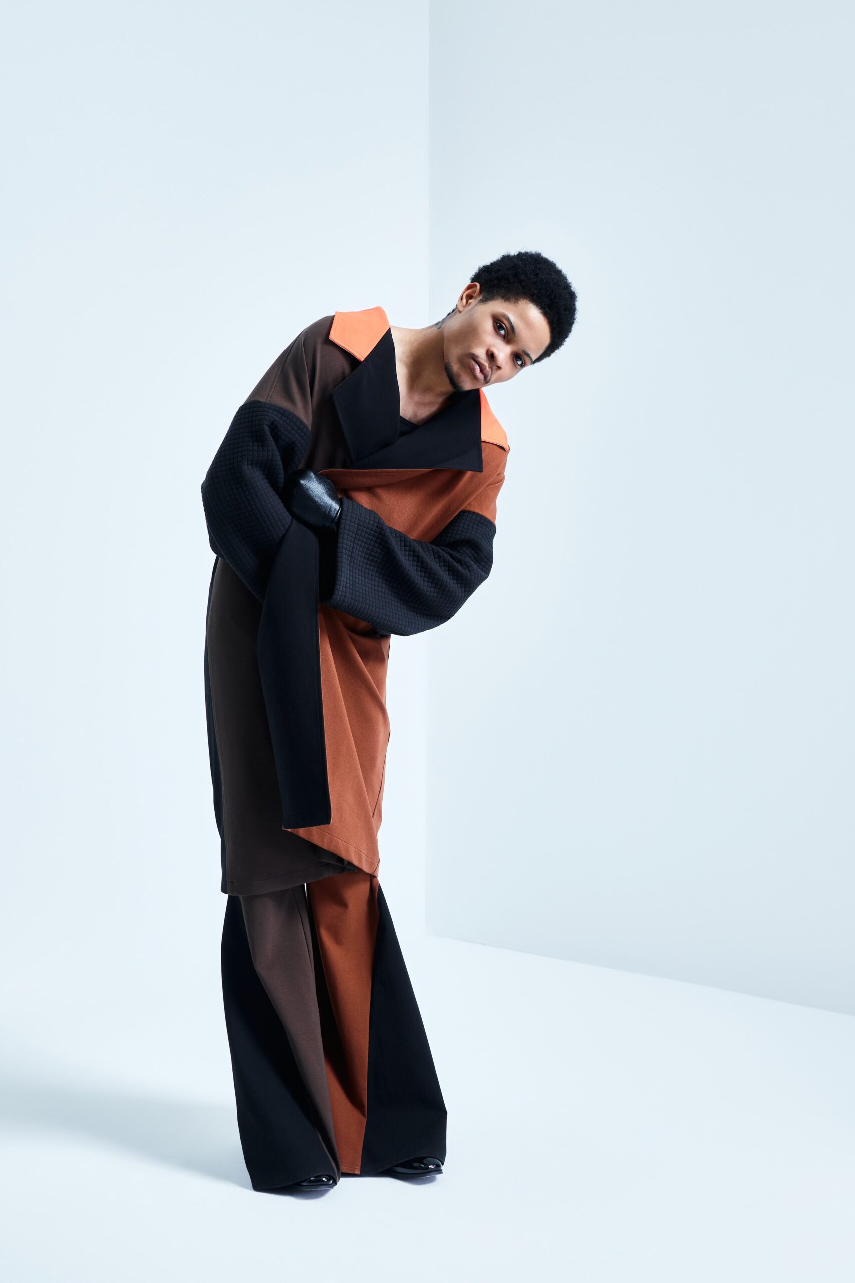 This relaxed coat features an asymmetric design, blending rich brown and black hues for a striking visual impact. Paired with wide-leg pants, the ensemble creates a fluid silhouette that emphasizes movement and modernity.