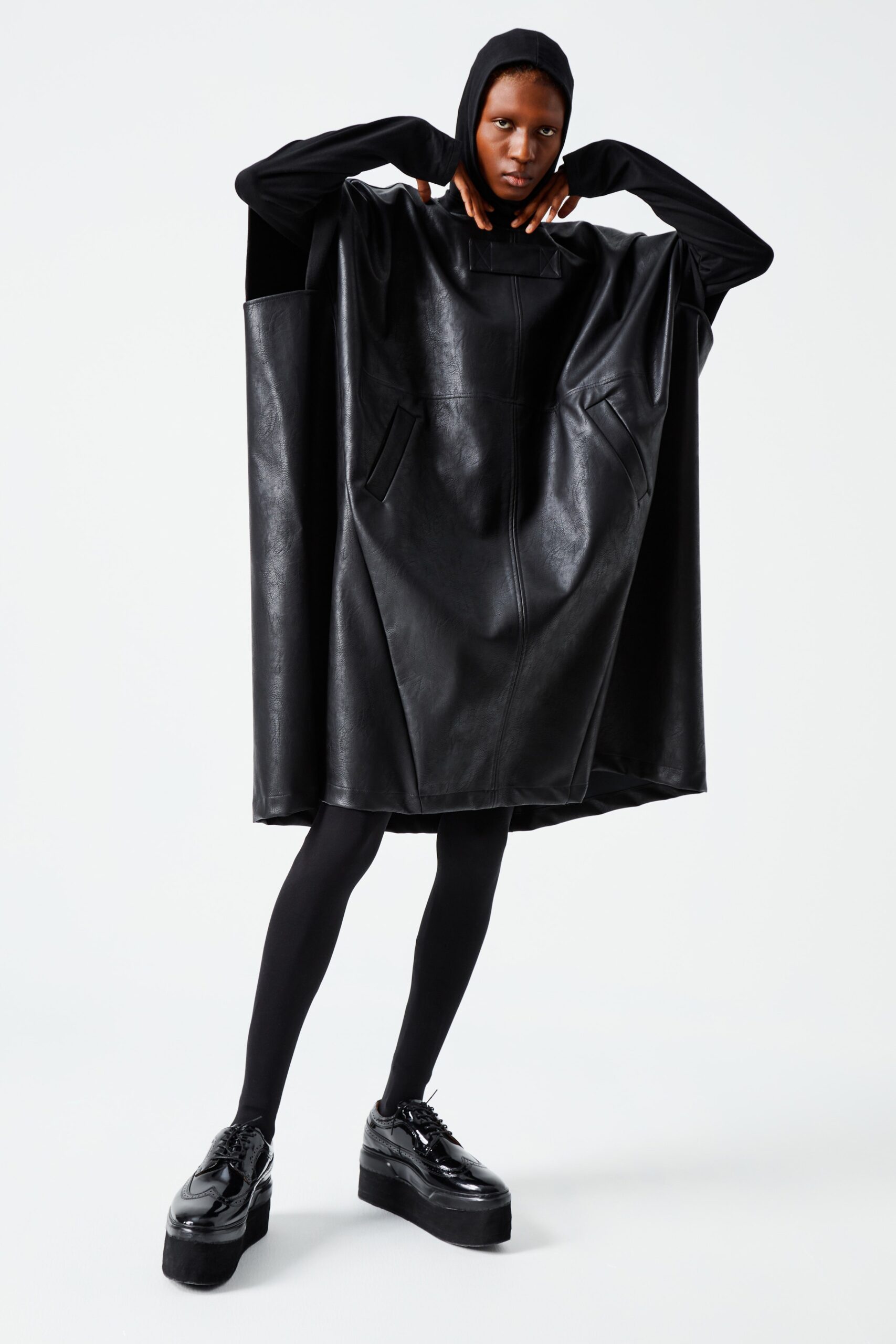 This oversized poncho in black leather features a unique hood and an asymmetric silhouette that challenges conventional shapes. The design emphasizes a bold, modern aesthetic, allowing for fluid movement while maintaining a striking presence.