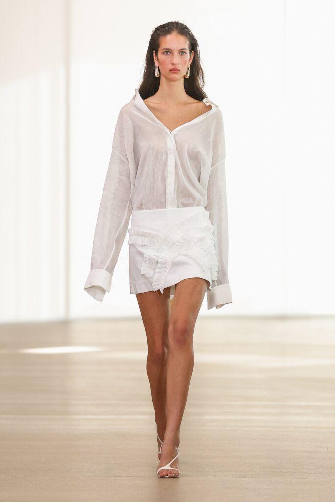 A relaxed white shirt with long sleeves and a collared neckline paired with a ruffled mini skirt.