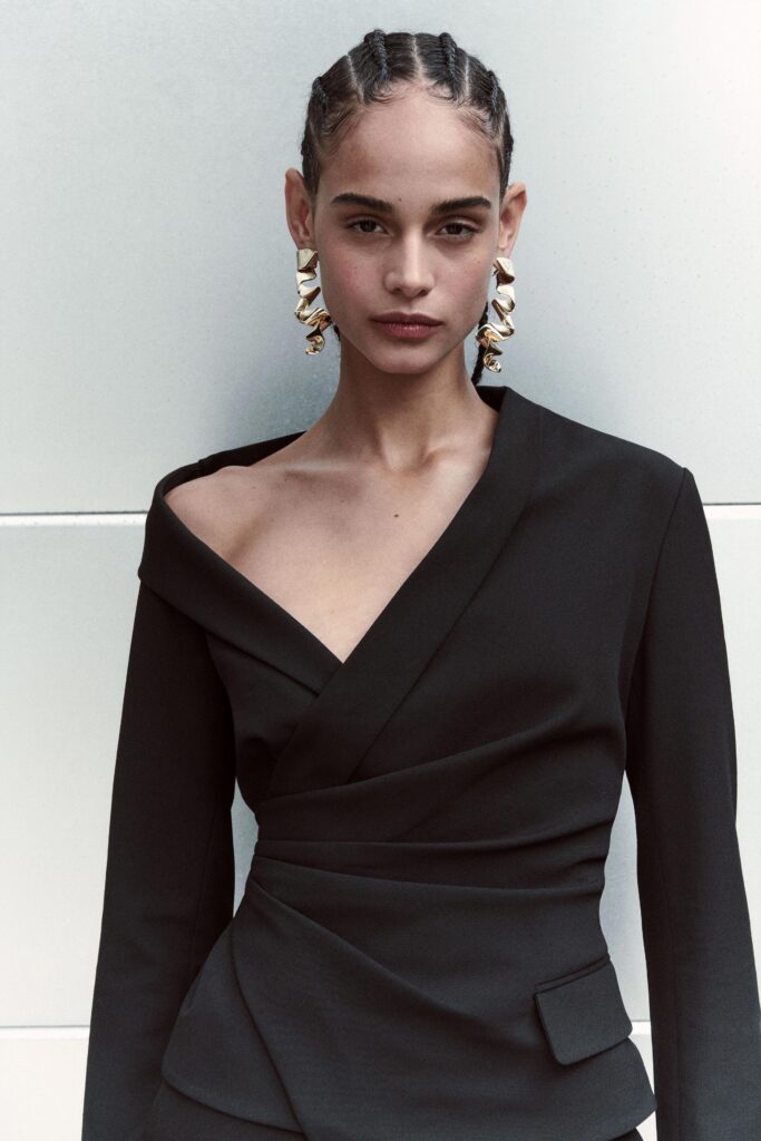 A fitted black cotton blazer with a V-neckline and asymmetric design detail.
