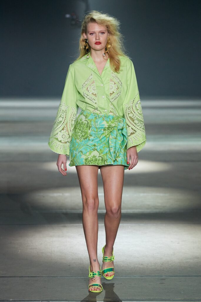A fitted green embroidered shirt with long sleeves paired with a flared blue skirt.