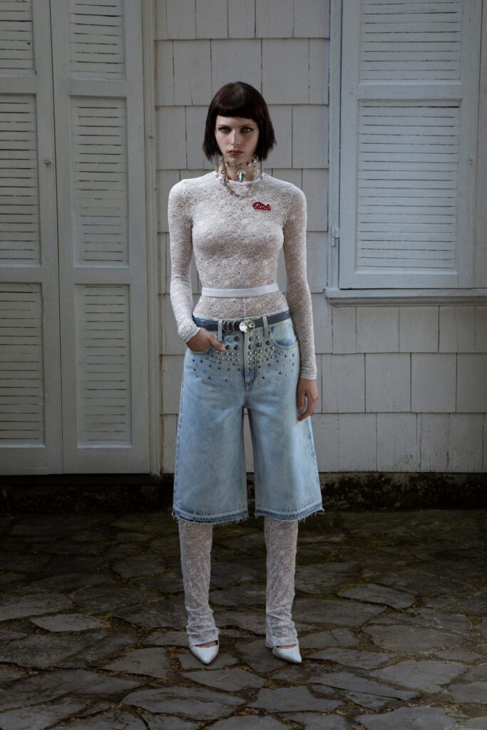 A fitted white lace long-sleeve top with a collar paired with wide-leg blue denim pants.