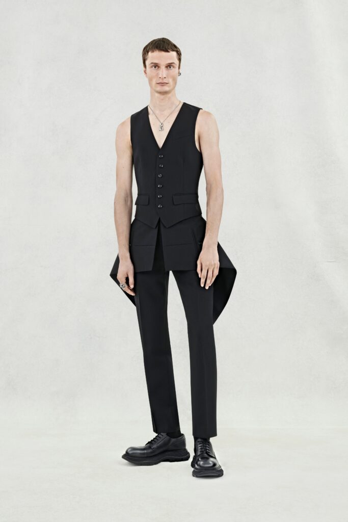 A fitted black sleeveless vest with a V-neck and asymmetric design paired with tailored pants.