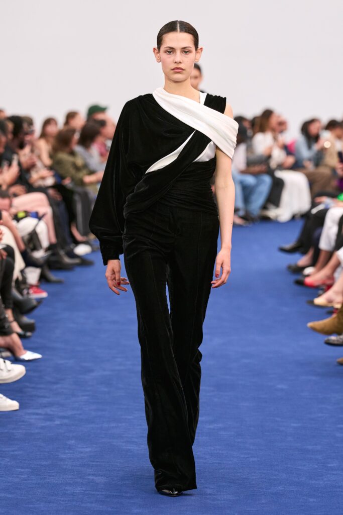 A fitted black velvet jumpsuit with long sleeves and an asymmetric design featuring white detailing.