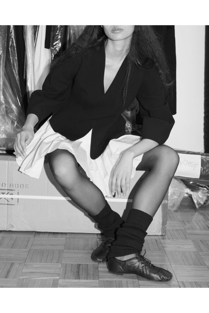 A fitted black jacket over a white pleated dress with a V-neckline and asymmetric design.