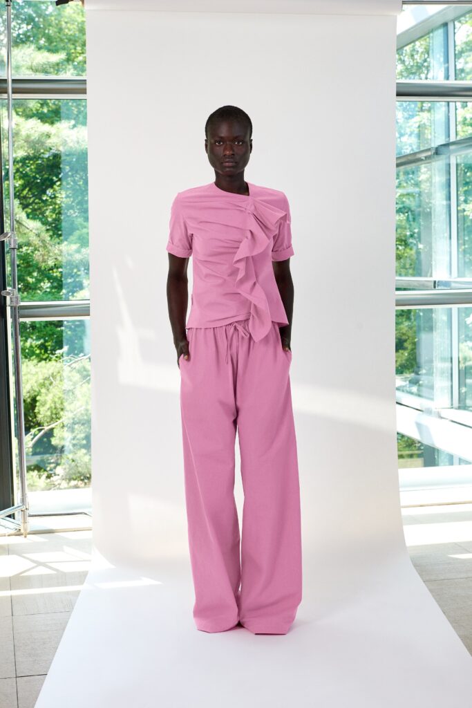A relaxed pink top with short sleeves and pleated details paired with wide-leg pants.