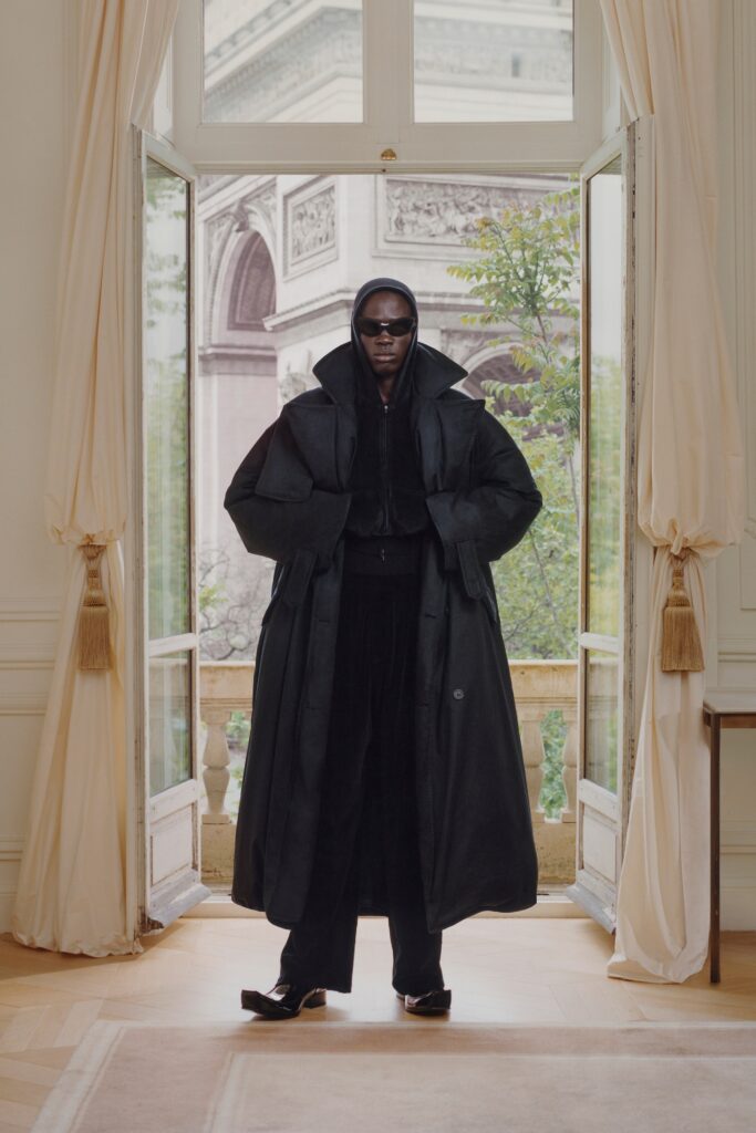 A relaxed black wool coat with a hood and zippered details, paired with matching pants.