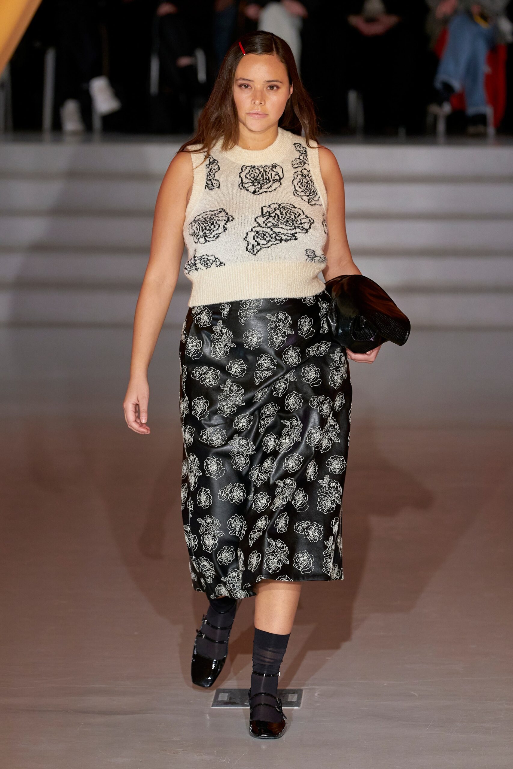 A fitted beige sleeveless top with a high neck paired with a black printed midi skirt.