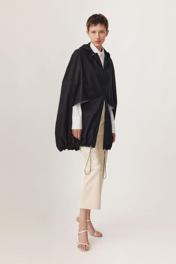 A relaxed black cape with long sleeves paired with beige cotton pants.
