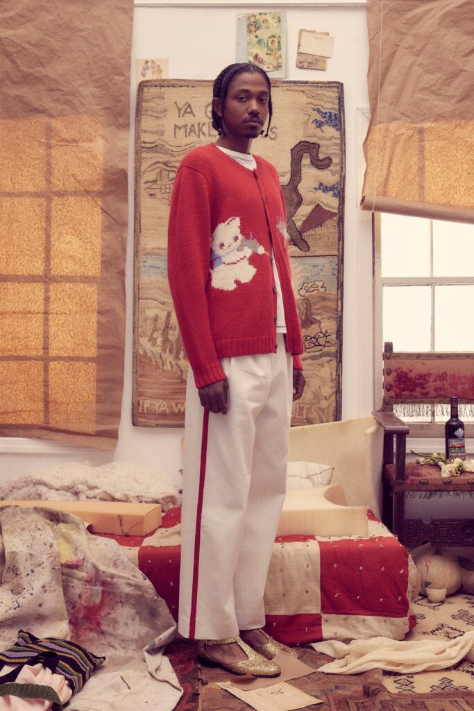 A relaxed red printed sweater with long sleeves paired with white pants.