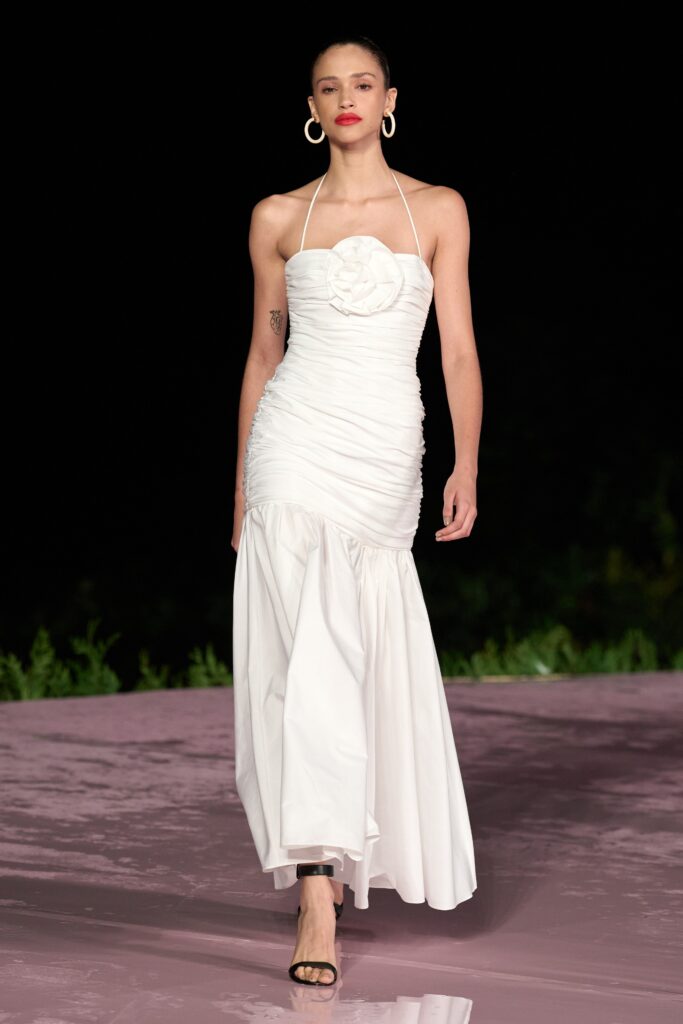 A fitted white halter dress with ruched detailing and a flowing maxi silhouette.