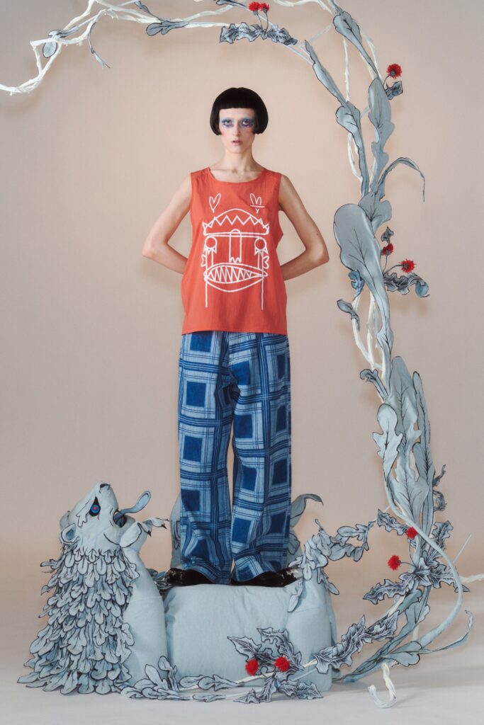 A relaxed orange sleeveless top with a printed design paired with wide-leg blue pants.
