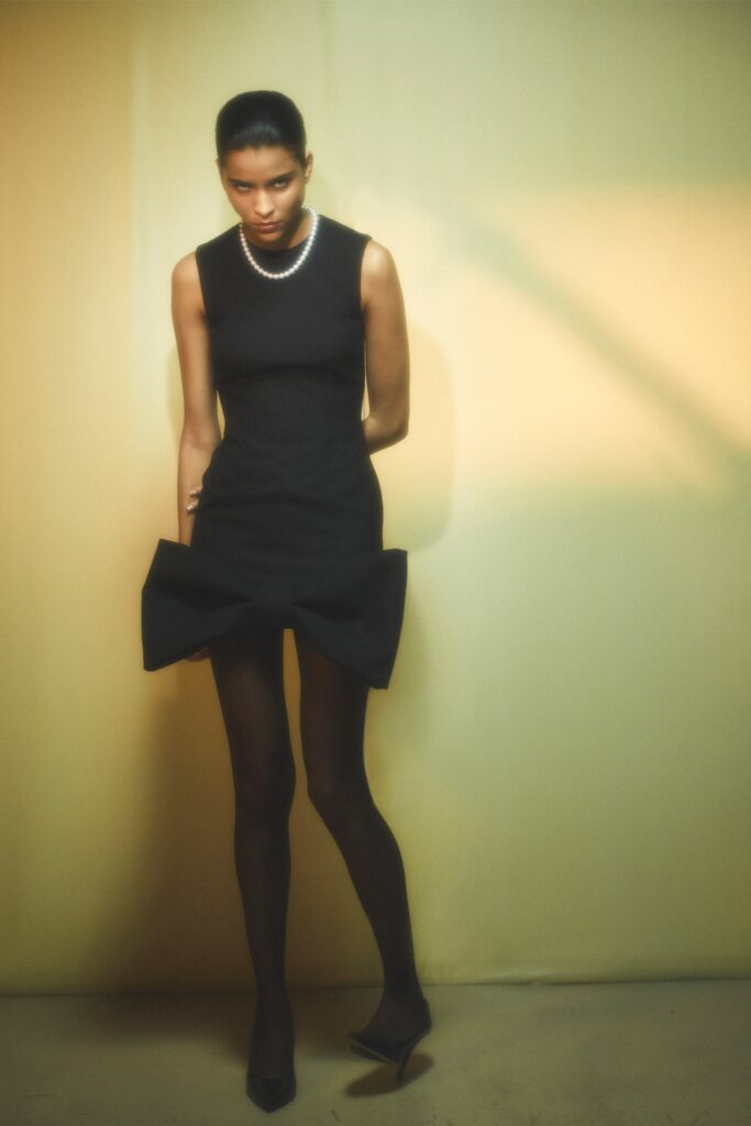 A fitted black sleeveless dress with an asymmetric design and high neckline.