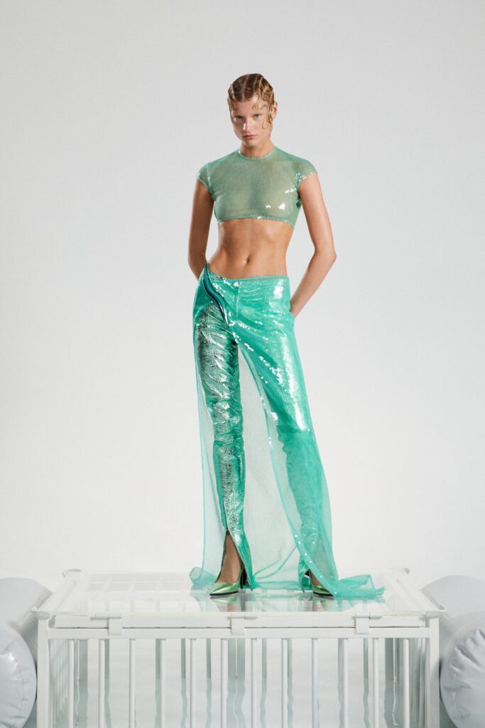 A fitted green sequin top with short sleeves paired with high-waisted pants featuring slits and layered design.