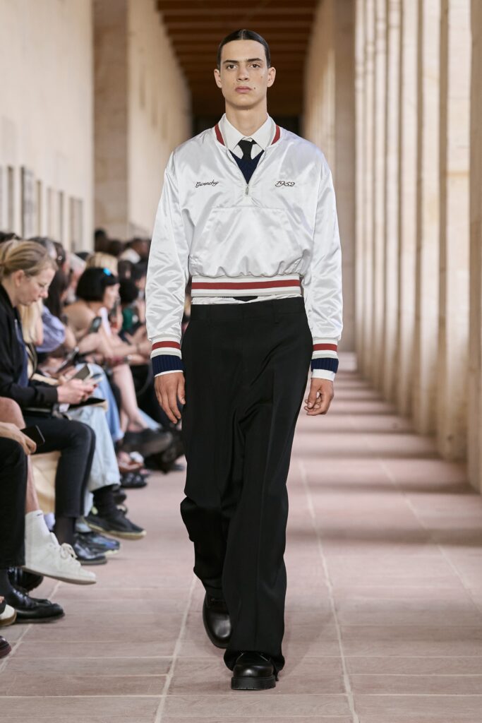 A fitted white satin jacket with long sleeves and a collared neckline paired with black pants.