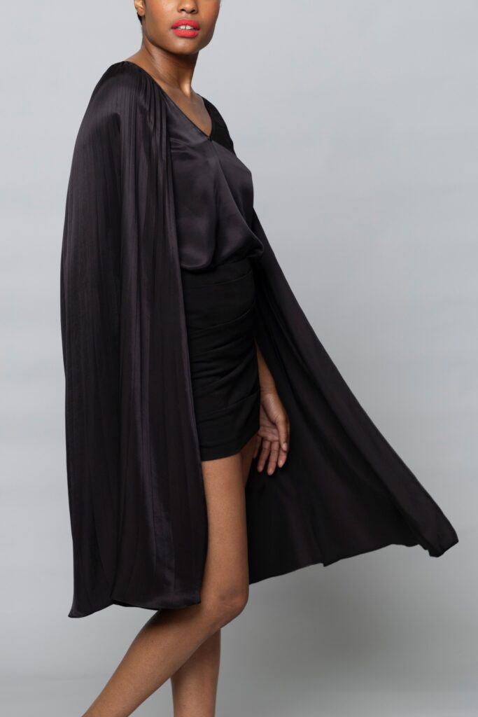 A fitted black silk dress with a V-neckline and an asymmetric cape detail.