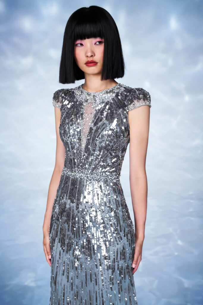 A fitted silver sequin gown with short sleeves and a V-neckline featuring a tiered design.