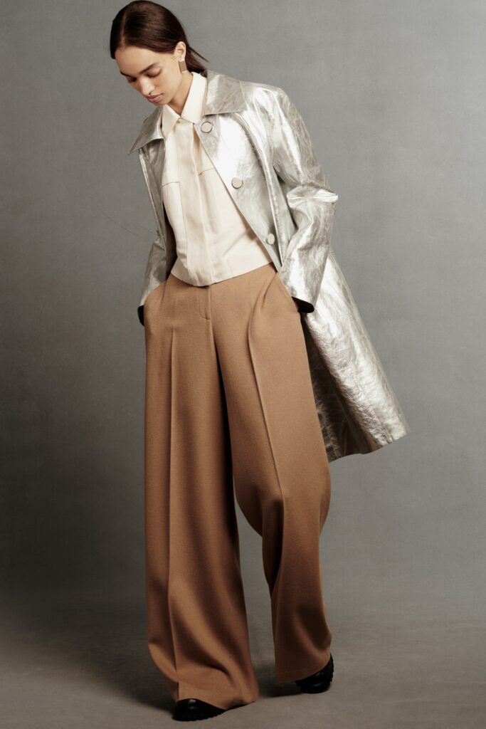 A relaxed silver leather coat paired with collared long-sleeve shirt and wide-leg brown pants.