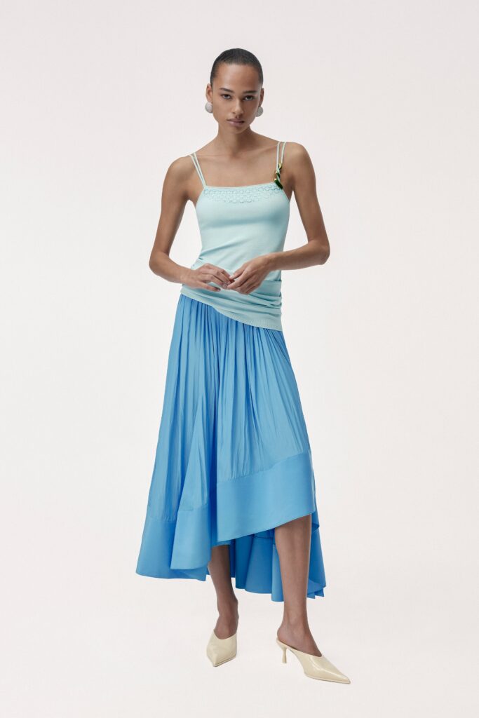 A fitted sleeveless top in aqua paired with a pleated asymmetric blue skirt.