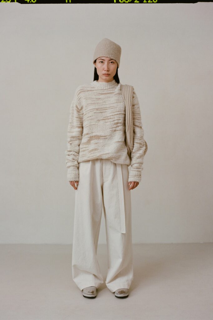 A relaxed beige sweater with long sleeves paired with white pants, featuring a textured design.