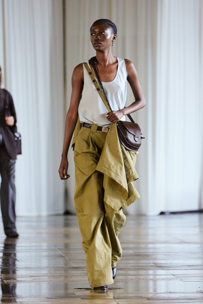 A relaxed white sleeveless top paired with high-waisted green pleated pants.