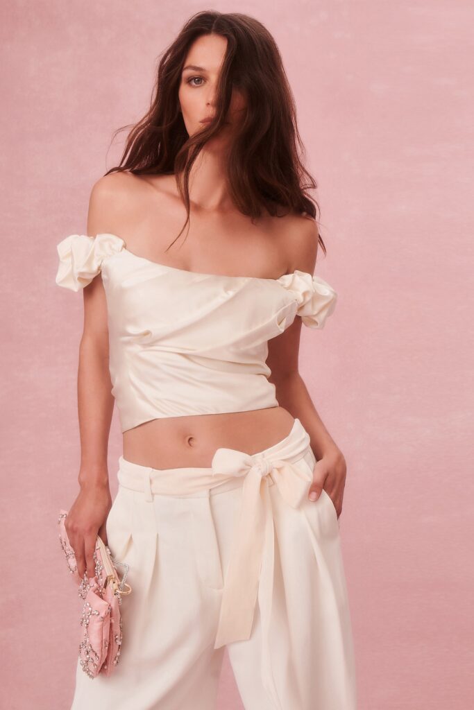 A fitted white silk off-shoulder top paired with pleated pants for a chic look.