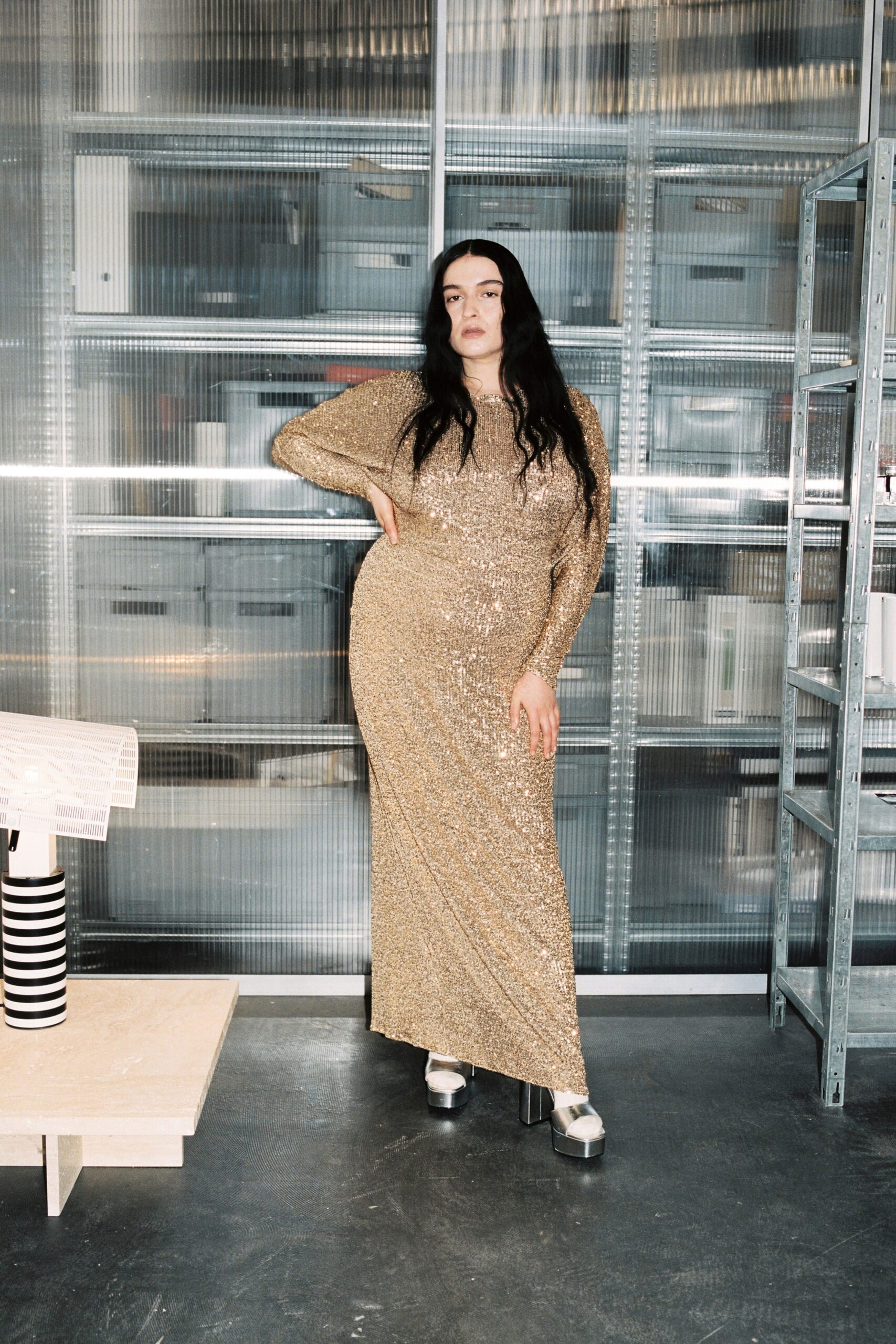 A fitted gold sequin gown with long sleeves and a V-neckline, featuring a maxi silhouette.