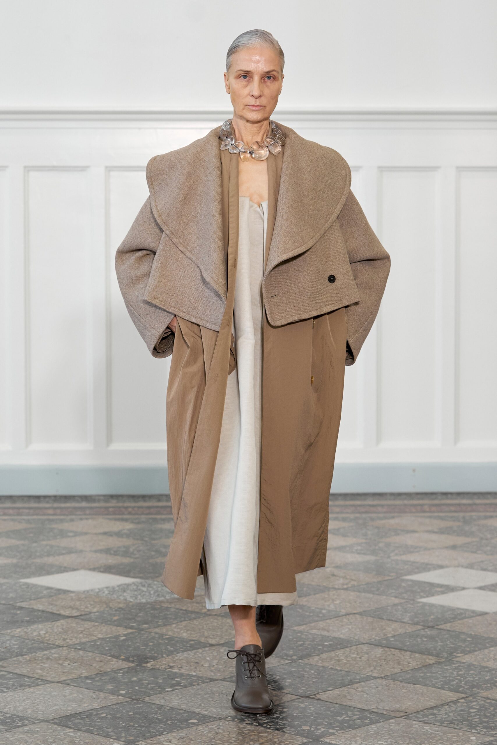 A relaxed brown wool coat layered over a beige dress with a collared neckline.