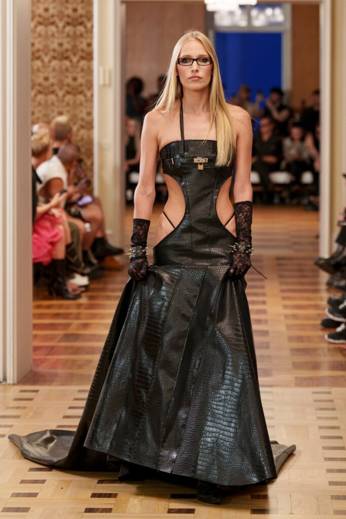A fitted black leather dress featuring dramatic cutouts and a floor-length hem.