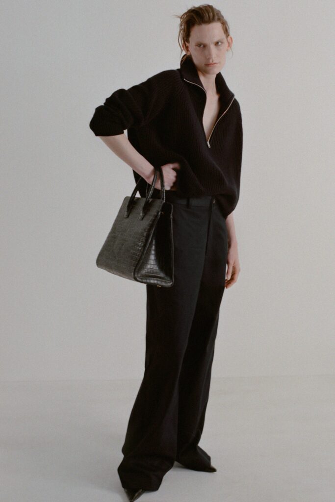 A relaxed black long-sleeve top with a zippered collar paired with black pants.