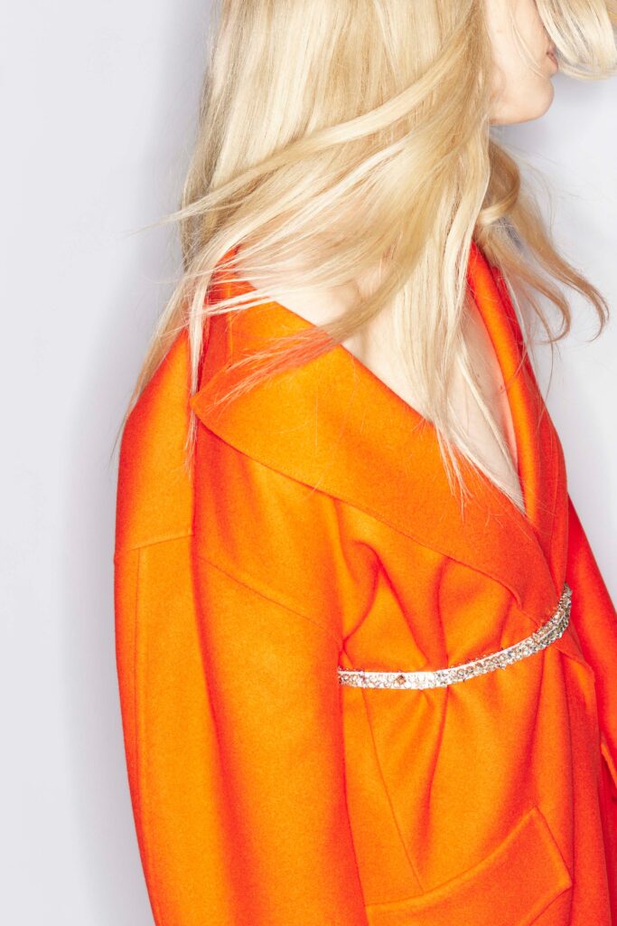 An oversized orange wool coat with a V-neckline and belted detail.