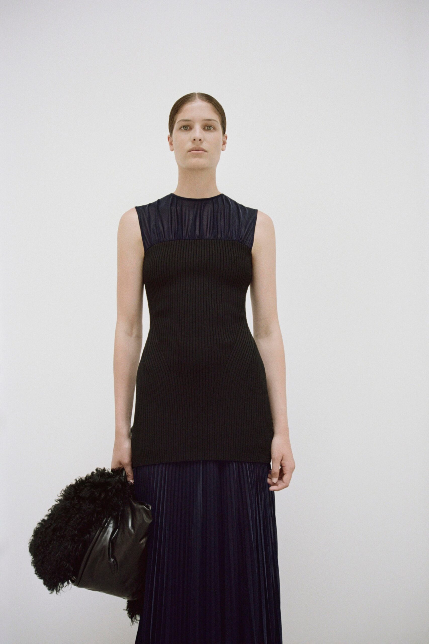 A fitted black silk sleeveless dress with a high neckline and pleated design.