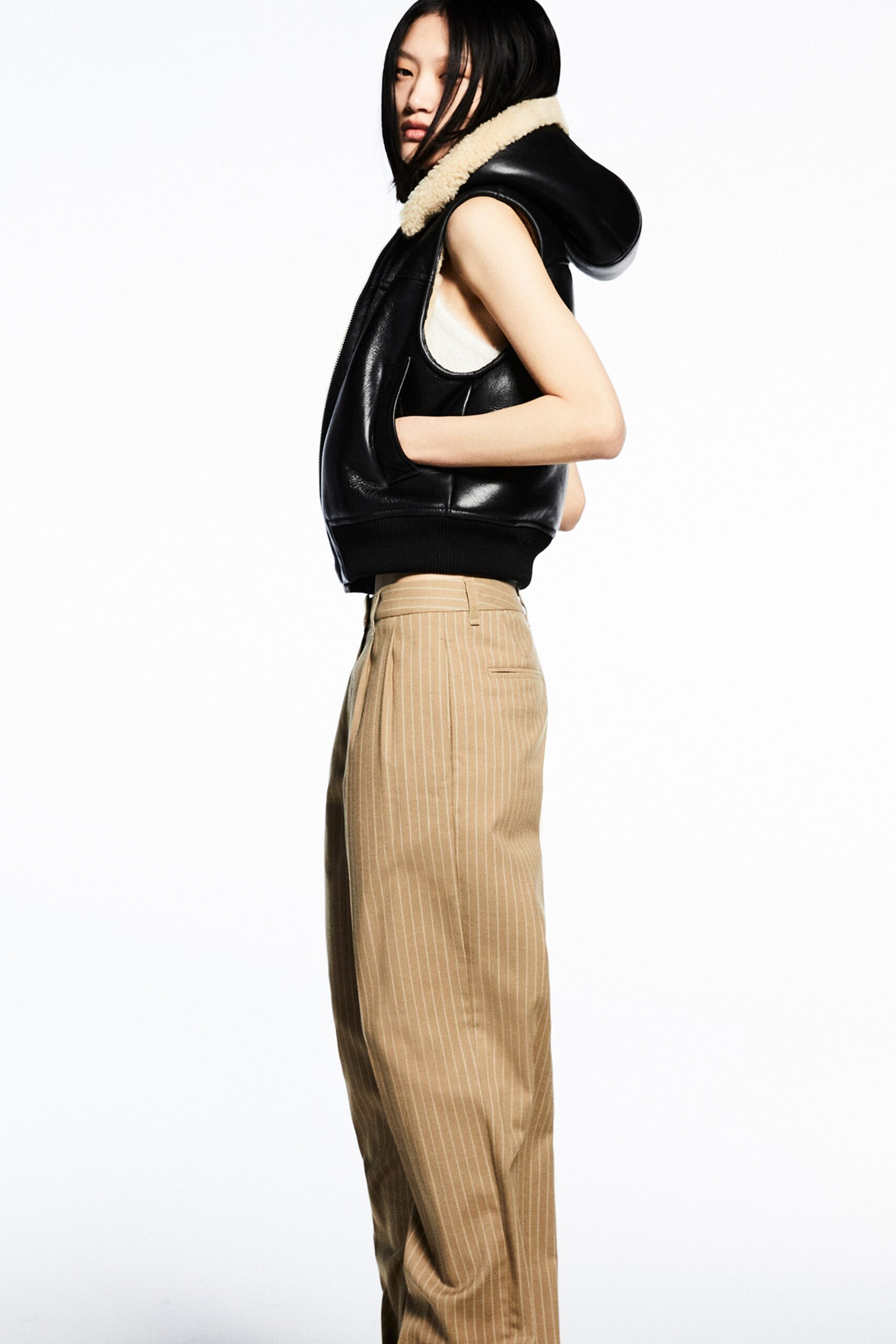 A fitted black leather sleeveless jacket paired with high-waisted beige striped pants.