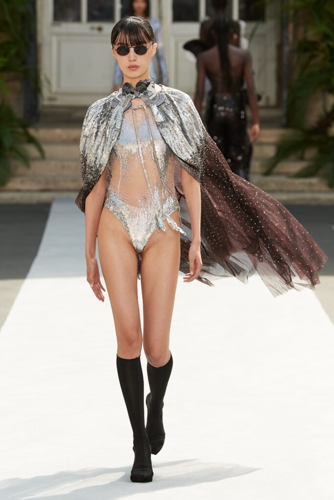 A fitted silver metallic swimsuit paired with an asymmetric tulle cape.