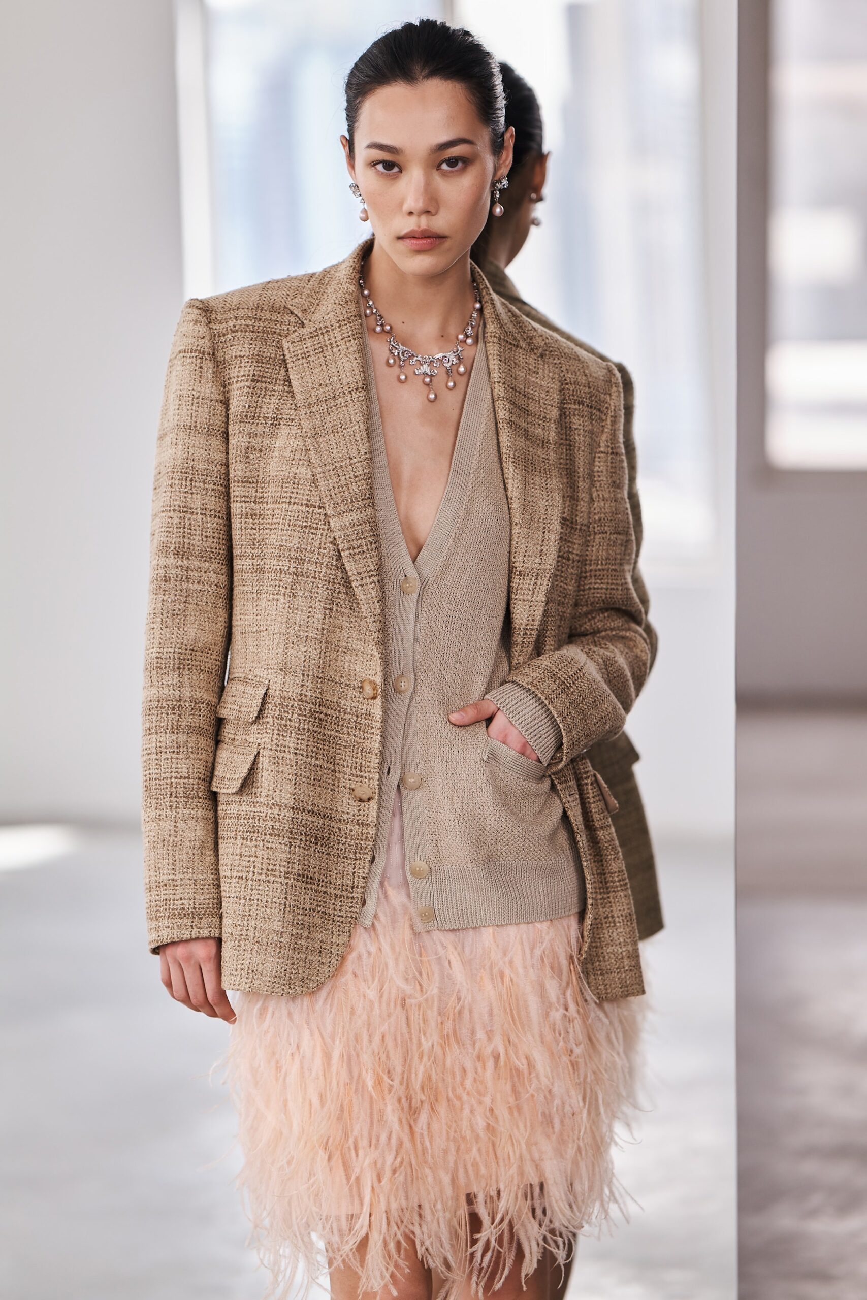 A fitted beige tweed blazer paired with a fringed pink skirt featuring a V-neckline.