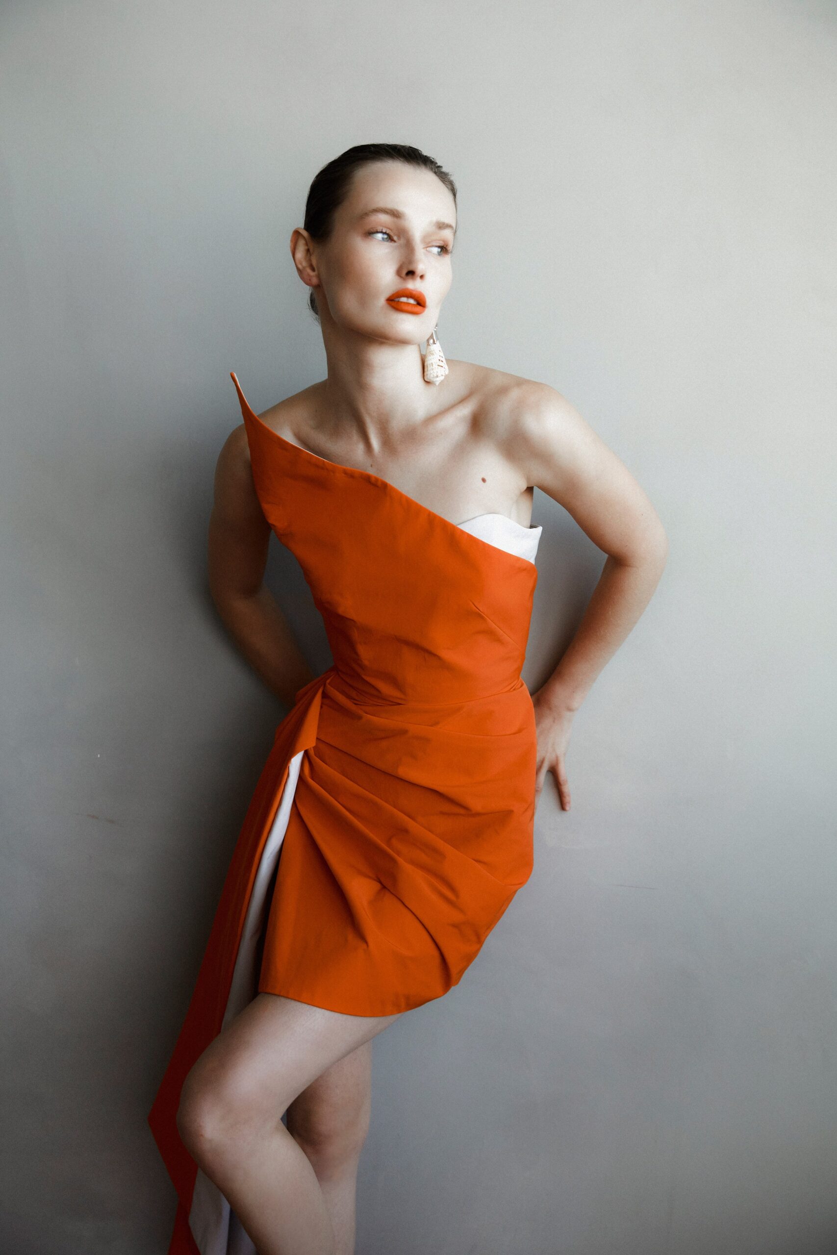 A fitted orange sleeveless dress with an asymmetric design and pleated detailing.