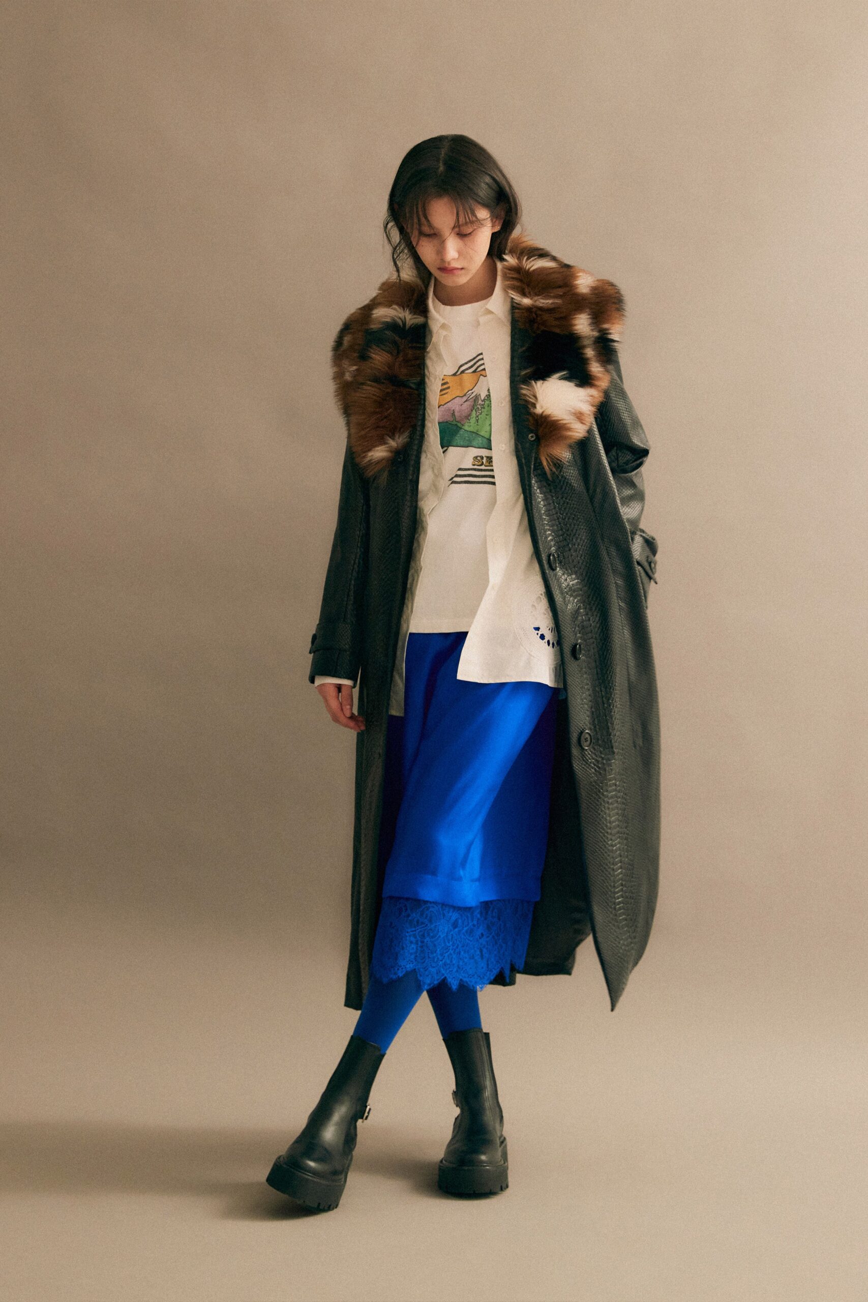 A relaxed black leather coat layered over a blue skirt with a collared long-sleeve shirt.