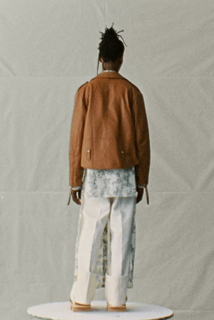 A relaxed brown leather jacket paired with white cotton pants, featuring a layered design.