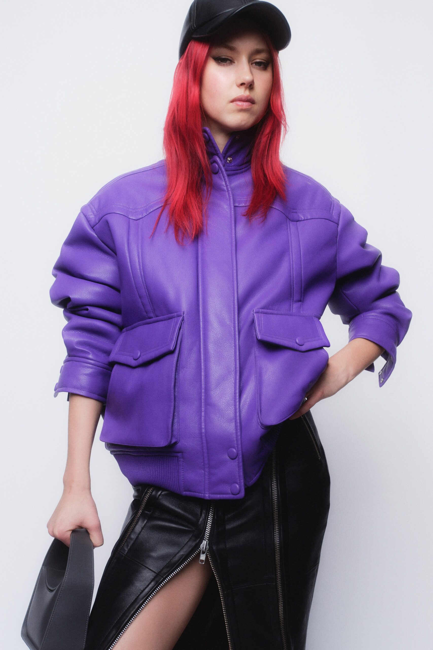 A fitted purple leather jacket with a collared design paired with a black skirt featuring a zippered slit.